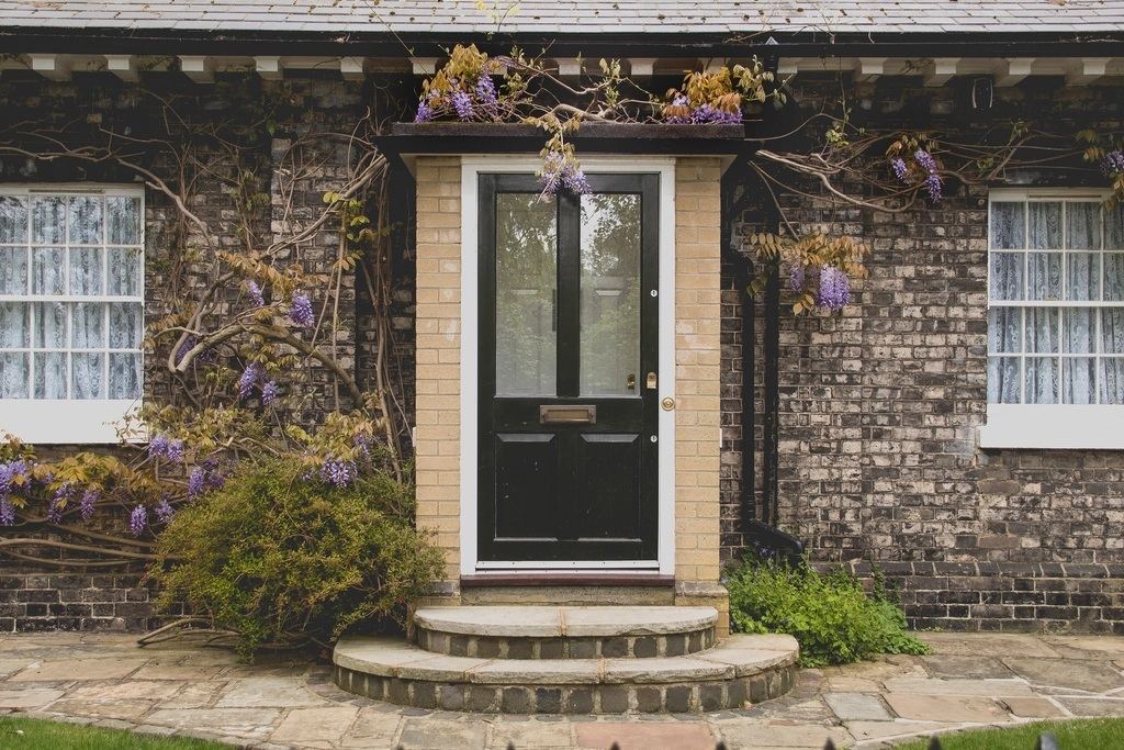 Front door of a period brick home framed by flowering wisteria