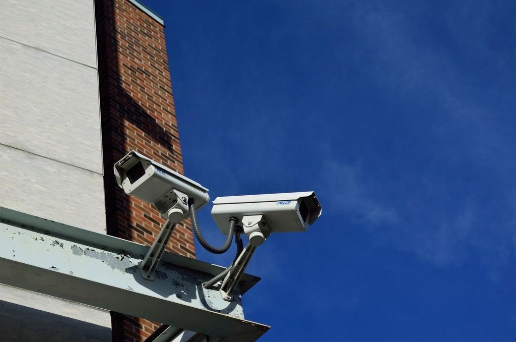 Two CCTV cameras mounted on a brick building against a blue sky